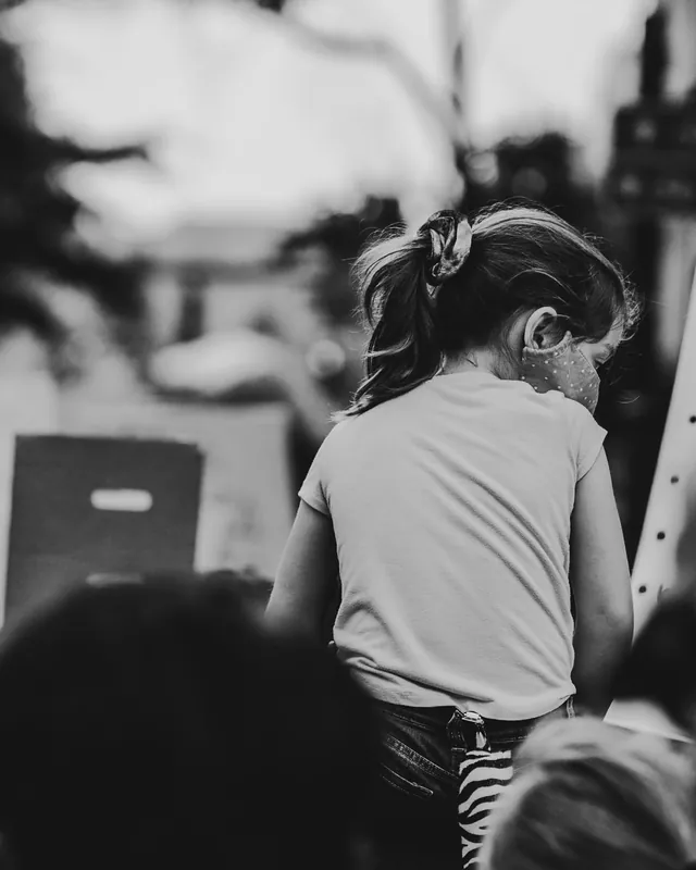 At a demonstration, a child sits on an adult's shoulders and looks into the crowd.
